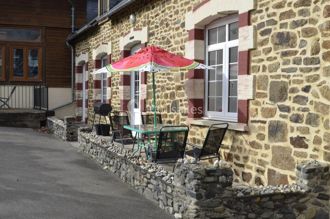 Façade en pierre avec terrasse équipée d'une table, chaises et parasol coloré en forme de pastèque.