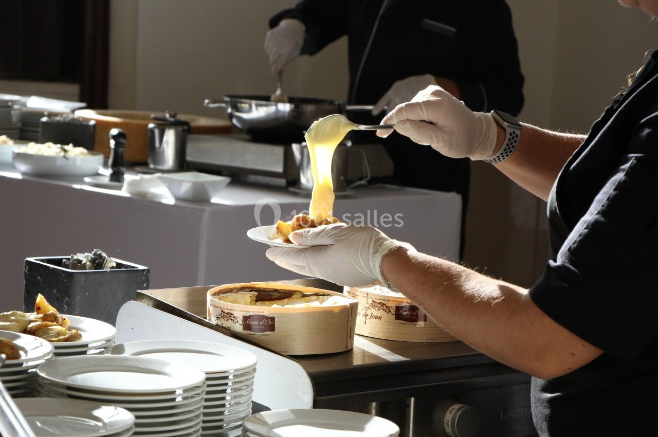 Une personne sert une sauce chaude sur un plat dans un buffet, avec des assiettes empilées au premier plan.