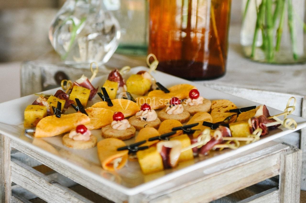 Plateau de bouchées apéritives variées, comprenant fruits, fromages et charcuteries, présenté sur une table en bois.