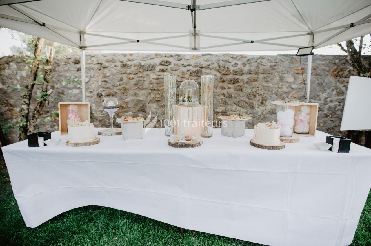Table décorée sous une tonnelle blanche avec gâteaux, fleurs et éléments décoratifs sur une nappe blanche.