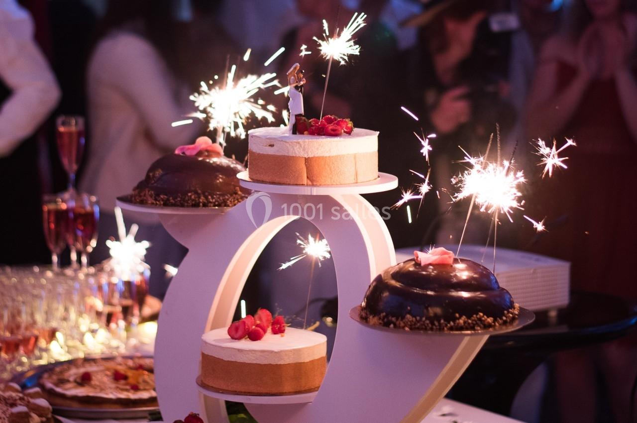 Gâteau de fête décoré de bougies et de cierges magiques, entouré de desserts et de convives en arrière-plan.