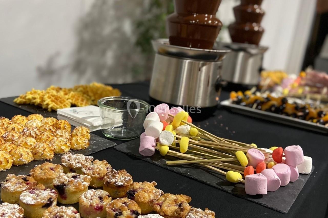 Table avec fontaine à chocolat, brochettes de guimauves, mini-gâteaux et pop-corn disposés pour un buffet dessert.