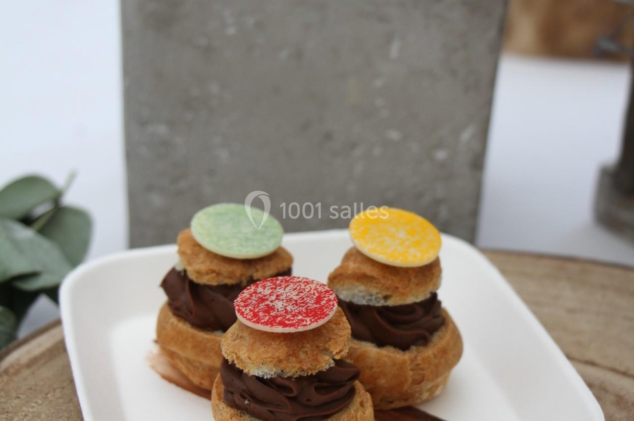 Assortiment de choux garnis de crème au chocolat, décorés de disques colorés, présentés sur une assiette blanche.