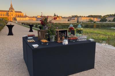 Gâteau de fête décoré de bougies scintillantes, entouré de desserts et de convives en arrière-plan flou.