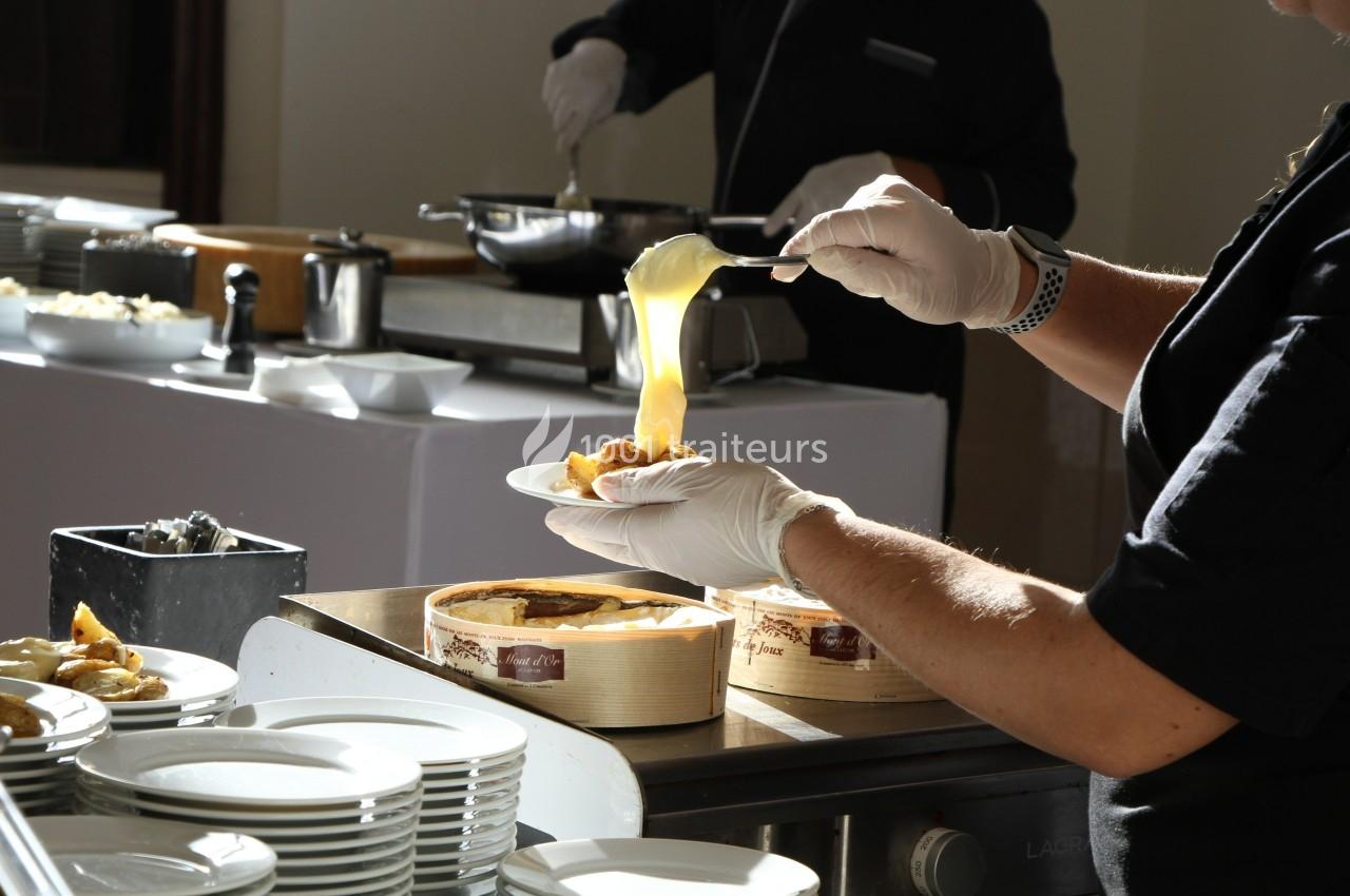 Une personne sert une sauce chaude sur un plat dans un buffet, avec des assiettes empilées au premier plan.