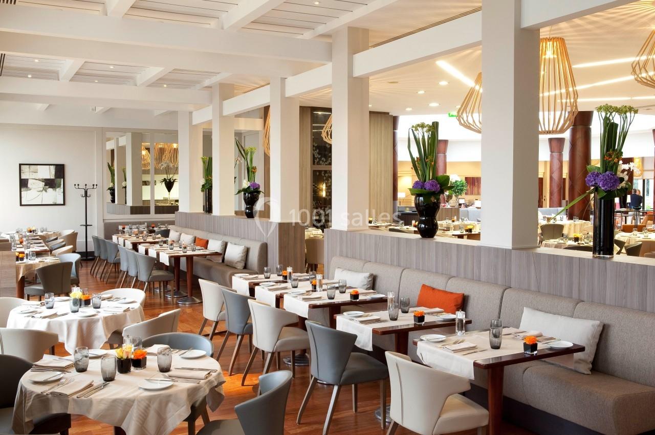 Salle de restaurant lumineuse avec tables dressées, chaises modernes et décorations florales.