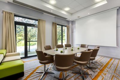 Salle de sport lumineuse avec tapis de course, vélos, haltères et coin détente avec fauteuils en osier.