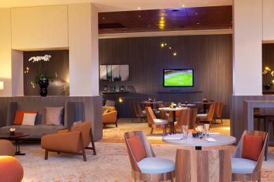 Salle de sport lumineuse avec tapis de course, vélos, haltères et coin détente avec fauteuils en osier.