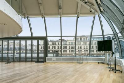 Vue d'une terrasse urbaine et d'un espace intérieur vitré avec parquet, offrant une perspective sur des bâtiments parisiens.