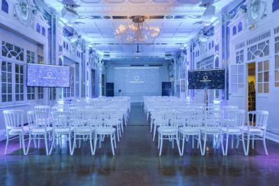 Salle lumineuse avec parquet en bois, murs blancs, mobilier noir et grandes fenêtres laissant entrer la lumière naturelle.