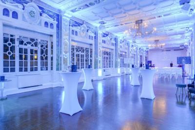 Salle lumineuse avec parquet en bois, murs blancs, mobilier noir et grandes fenêtres laissant entrer la lumière naturelle.