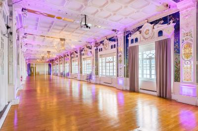 Salle lumineuse avec parquet en bois, murs blancs, mobilier noir et grandes fenêtres laissant entrer la lumière naturelle.