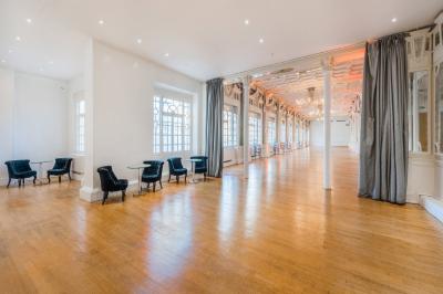 Salle lumineuse avec parquet en bois, murs blancs, mobilier noir et grandes fenêtres laissant entrer la lumière naturelle.