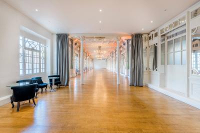 Salle lumineuse avec parquet en bois, murs blancs, mobilier noir et grandes fenêtres laissant entrer la lumière naturelle.