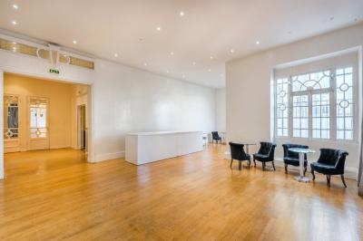 Salle lumineuse avec parquet en bois, murs blancs, mobilier noir et grandes fenêtres laissant entrer la lumière naturelle.