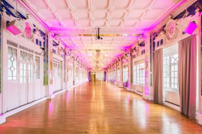 Salle lumineuse avec parquet en bois, murs blancs, mobilier noir et grandes fenêtres laissant entrer la lumière naturelle.