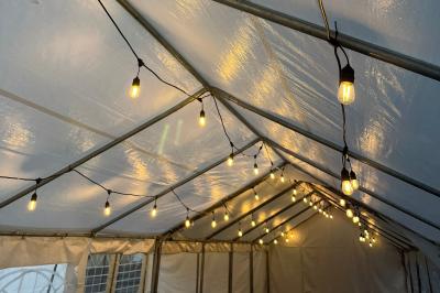 Guirlandes lumineuses suspendues sous une tente blanche avec une toile translucide.