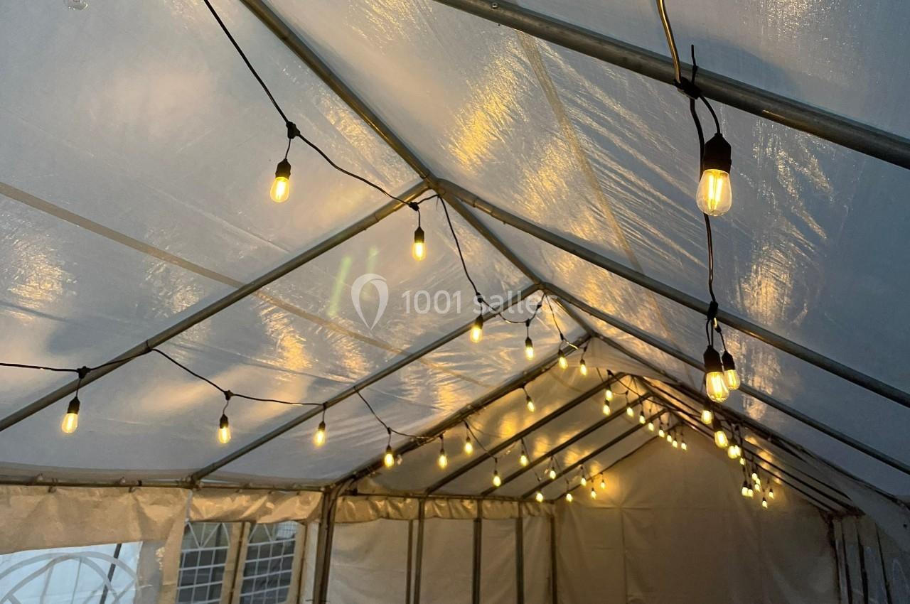 Guirlandes lumineuses suspendues sous une tente blanche avec une toile translucide.