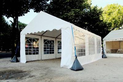 Tente blanche avec parois transparentes installée en extérieur sur un sol gravillonné, entourée d'arbres.