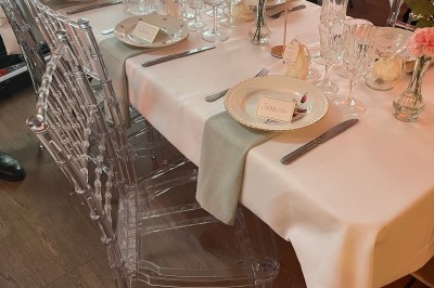 Tente blanche avec parois transparentes installée en extérieur sur un sol gravillonné, entourée d'arbres.