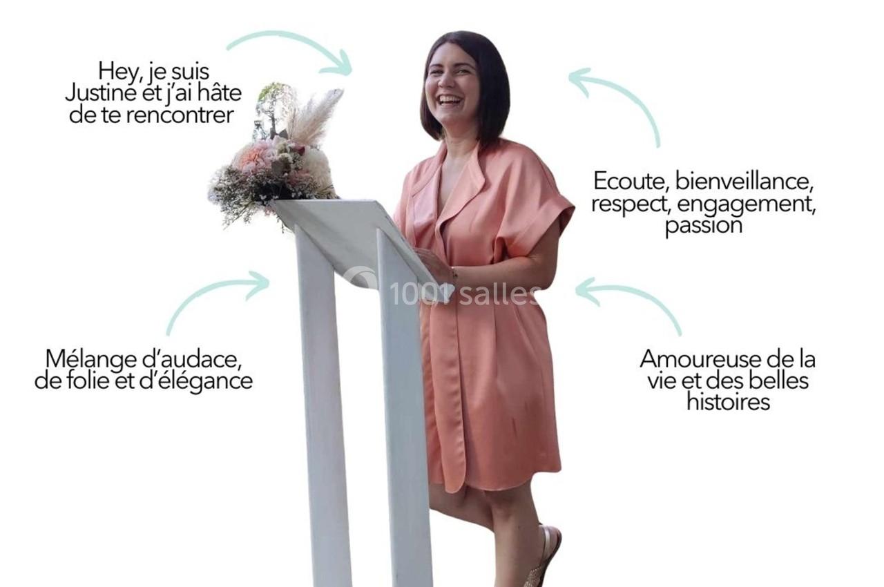 Femme souriante en robe rose debout derrière un pupitre décoré de fleurs séchées.