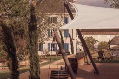 Façade d'une maison ancienne avec volets bleus, entourée de végétation et éclairée par des guirlandes lumineuses.