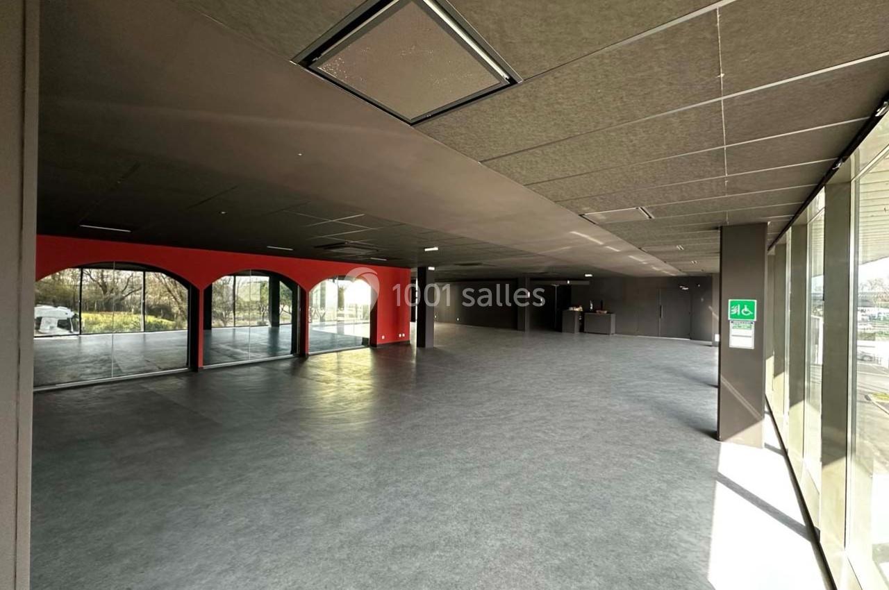 Intérieur d'un espace vide avec sol gris, murs sombres, grandes baies vitrées et lumière naturelle entrant.