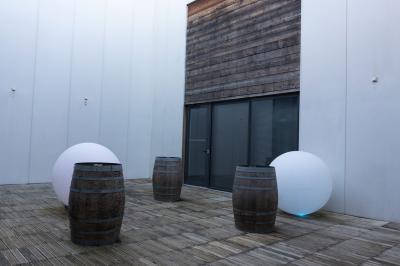 Cour intérieure avec sol en bois, quatre tonneaux et deux grandes sphères blanches près d'un mur et d'une porte vitrée.