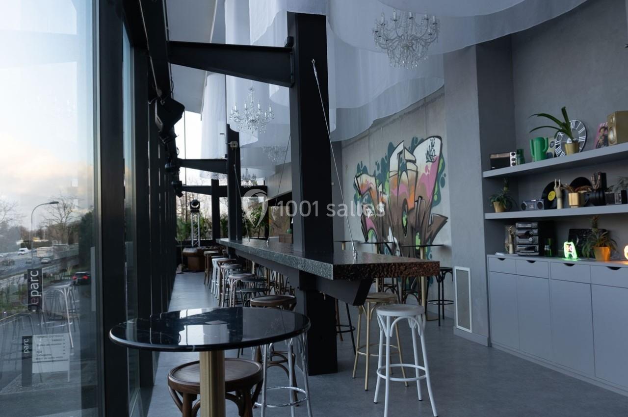 Intérieur d'un café moderne avec un long comptoir, des tabourets, des étagères décorées et une fresque murale colorée.