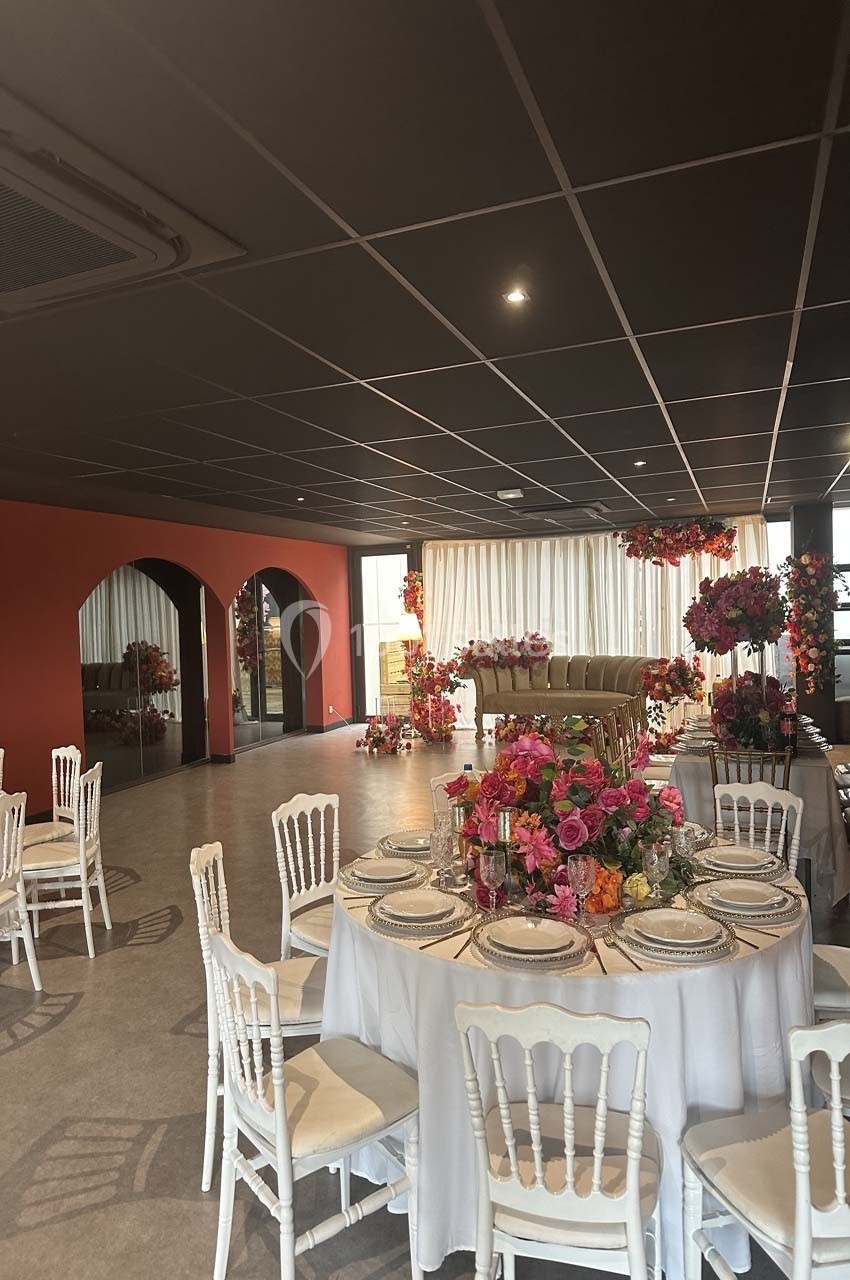 Salle de réception décorée avec des tables rondes, des chaises blanches et des arrangements floraux colorés.