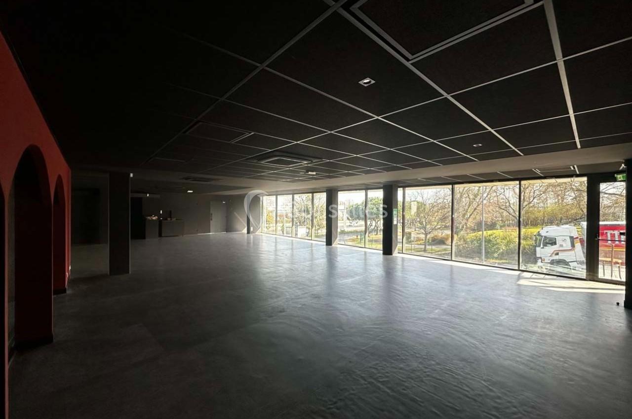 Salle spacieuse avec de grandes baies vitrées laissant entrer la lumière naturelle, vue sur un espace extérieur arboré.