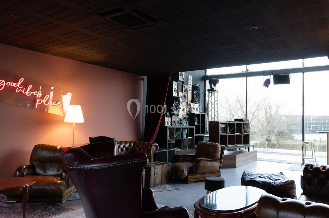 Salon moderne avec fauteuils en cuir, lampadaire, enseigne néon ’good vibes only’ et grande baie vitrée donnant sur l…