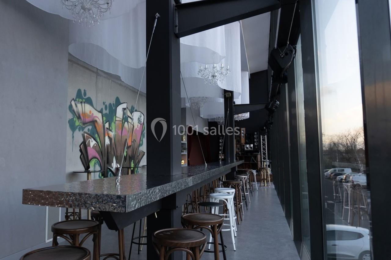 Intérieur d'un bar moderne avec un long comptoir métallique, des tabourets et une fresque murale colorée.