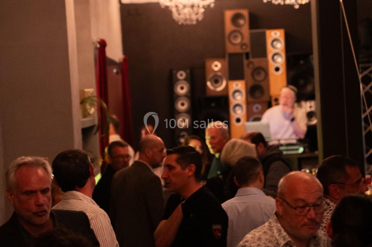 Groupe de personnes discutant dans une salle avec des enceintes empilées en arrière-plan et un DJ à une table de mixage.