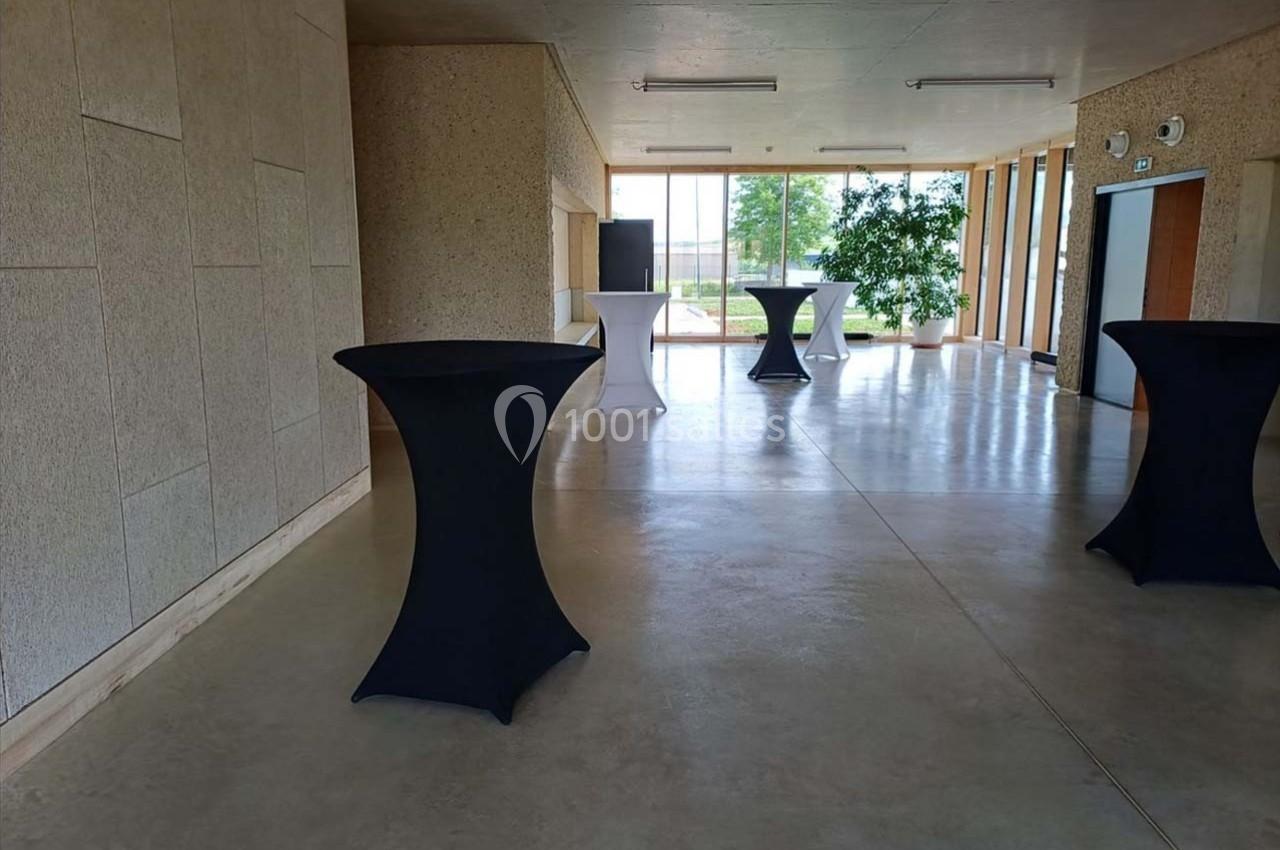 Salle lumineuse avec tables hautes noires et blanches, grandes fenêtres et plantes en arrière-plan.