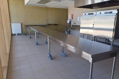 Cuisine professionnelle avec plans de travail en inox sur roulettes, four industriel et carrelage au sol.