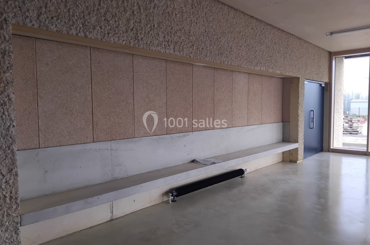 Banc en béton intégré à un mur texturé, dans un espace intérieur lumineux avec une porte bleue et une fenêtre.