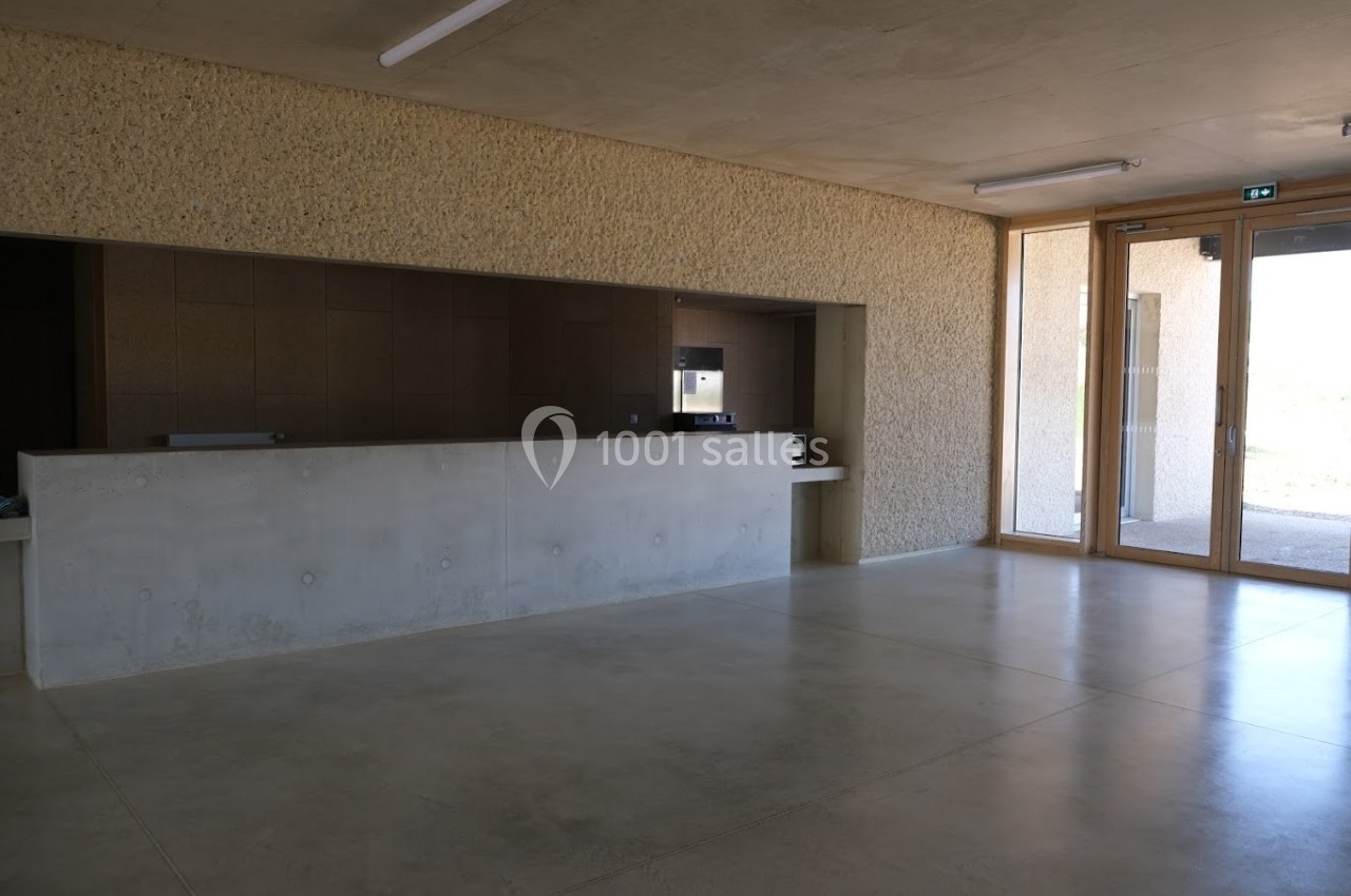 Un comptoir en béton dans un espace intérieur minimaliste avec sol en béton, murs texturés et grande porte vitrée.