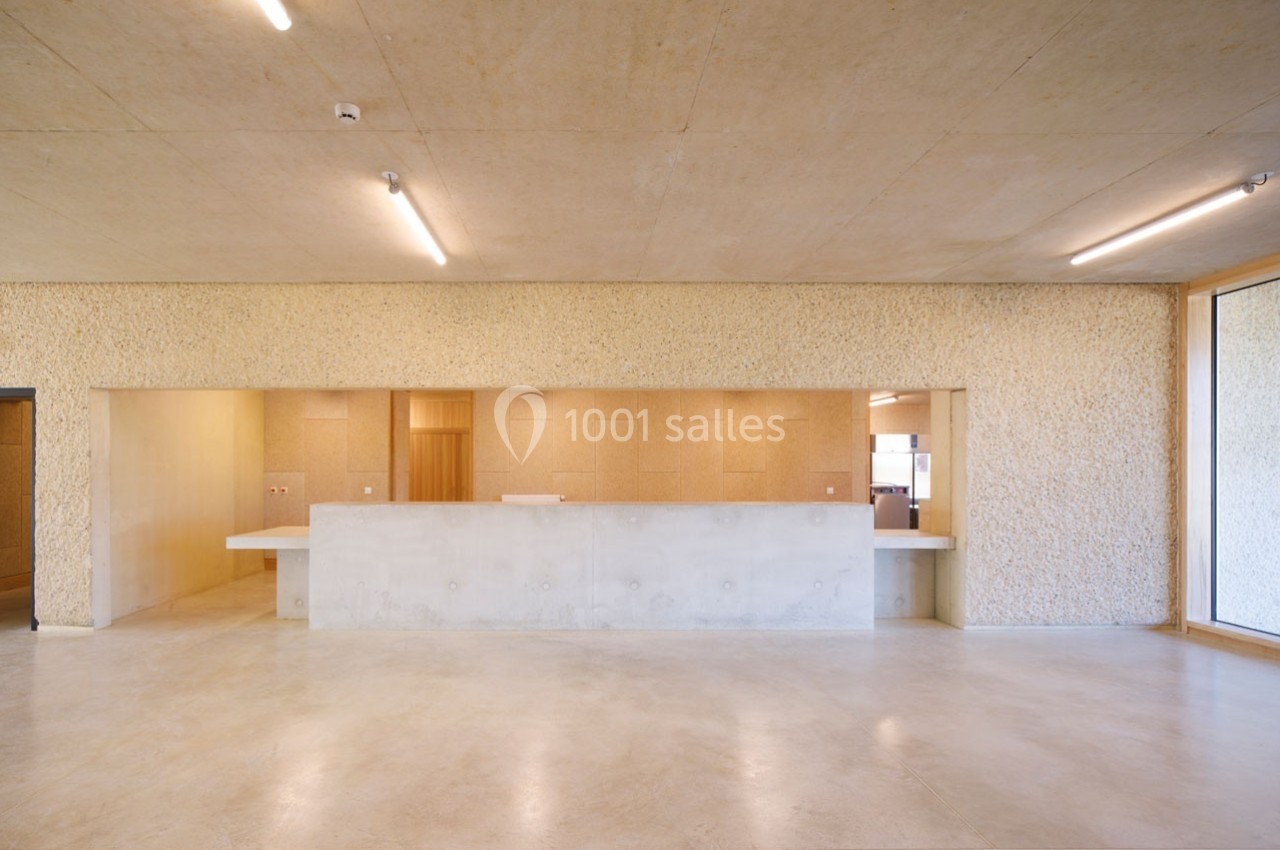 Hall avec comptoir en béton, murs texturés clairs et éclairage fluorescent, donnant sur une pièce lumineuse.