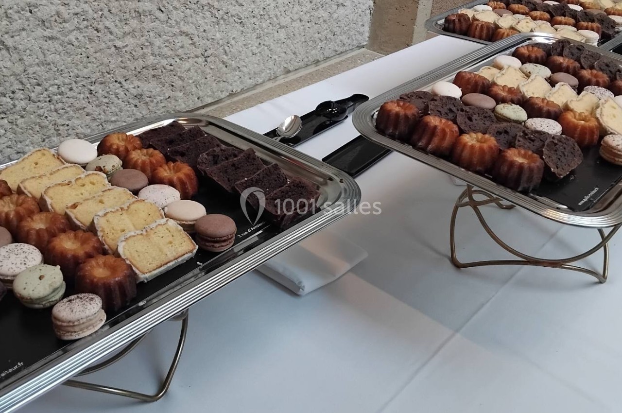 Plateaux de pâtisseries variées, incluant cannelés, macarons et tranches de gâteaux, disposés sur une table blanche.