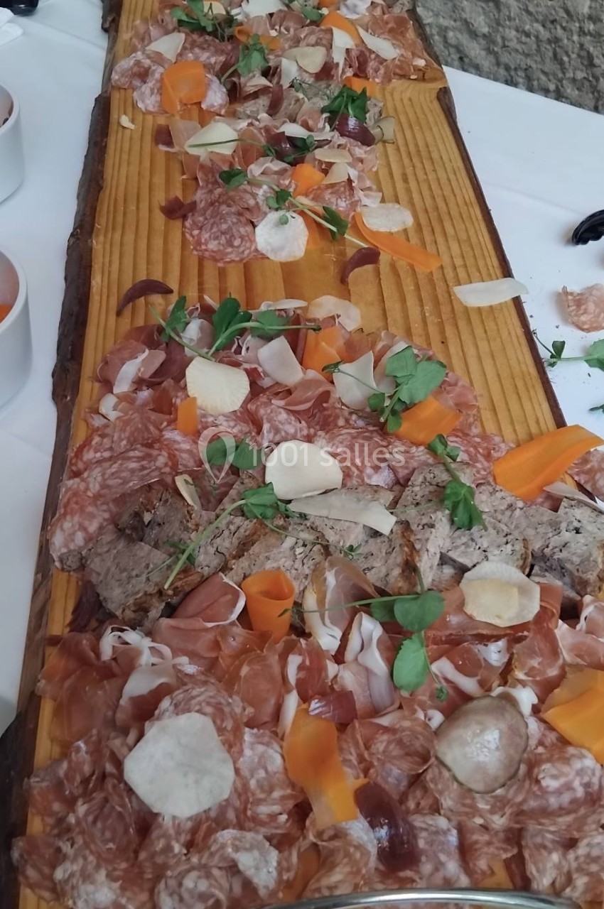 Plateau en bois garni de charcuteries variées, tranches de légumes, herbes fraîches et copeaux de fromage.