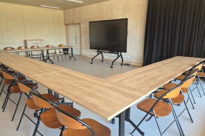Paysage rural avec des champs cultivés, une maison isolée et une forêt en arrière-plan sous un ciel bleu.