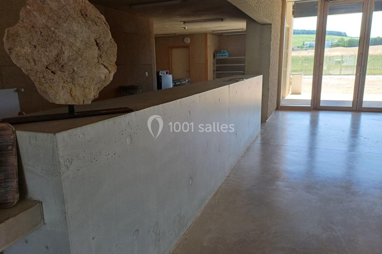 Comptoir en béton dans un espace intérieur lumineux avec une grande baie vitrée donnant sur un paysage rural.