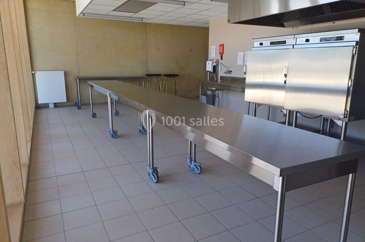 Cuisine professionnelle avec plans de travail en inox sur roulettes, four industriel et carrelage au sol.