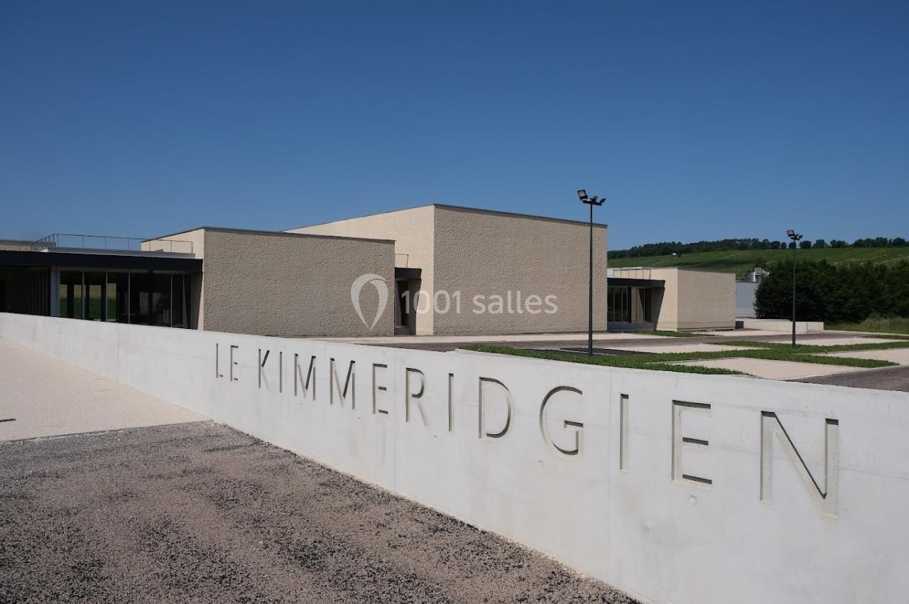 Bâtiment moderne beige avec l'inscription ’Le Kimméridgien’ sur un mur blanc, sous un ciel bleu dégagé.