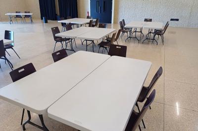 Paysage rural avec des champs cultivés, une maison isolée et une forêt en arrière-plan sous un ciel bleu.