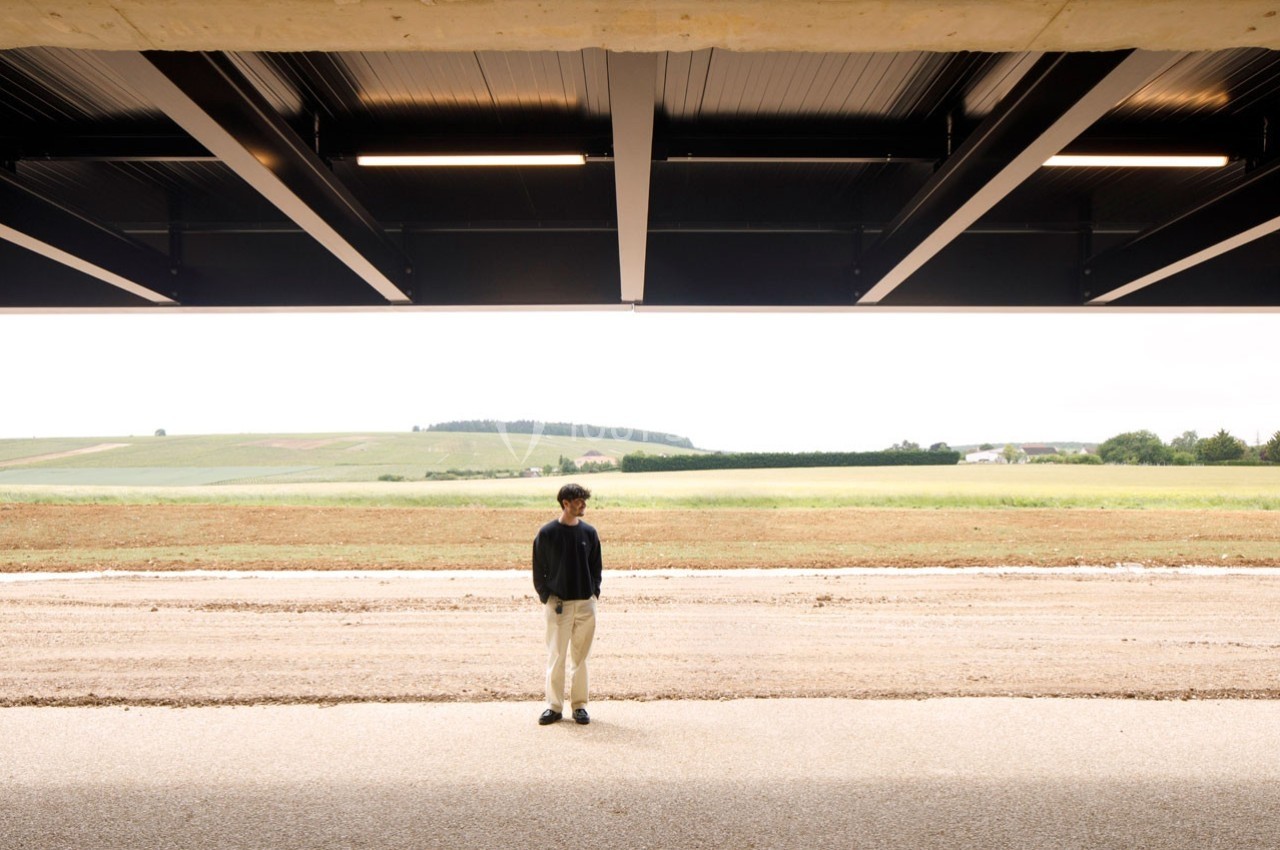 Un homme debout sous une structure moderne en métal, avec un paysage rural en arrière-plan.