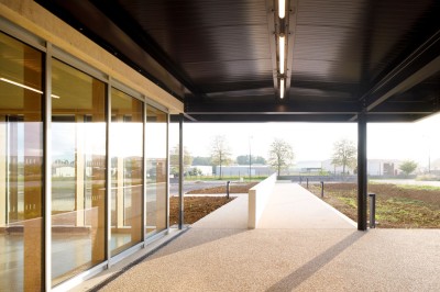 Paysage rural avec des champs cultivés, une maison isolée et une forêt en arrière-plan sous un ciel bleu.