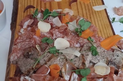 Plateau en bois garni de charcuteries variées, tranches de légumes et herbes fraîches, présenté sur une table blanche.