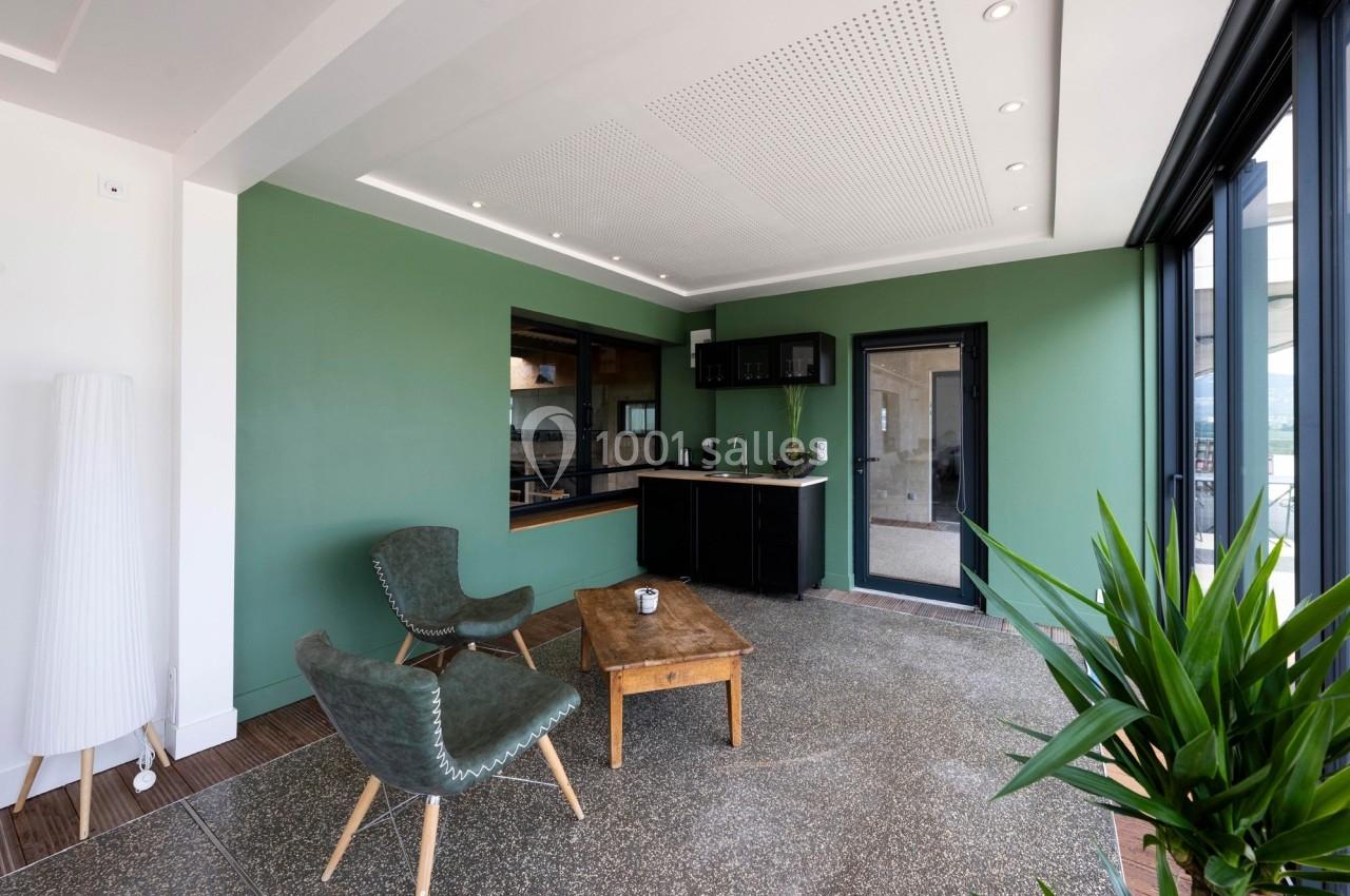 Espace intérieur lumineux avec murs verts, coin cuisine noir, table basse en bois et fauteuils verts.